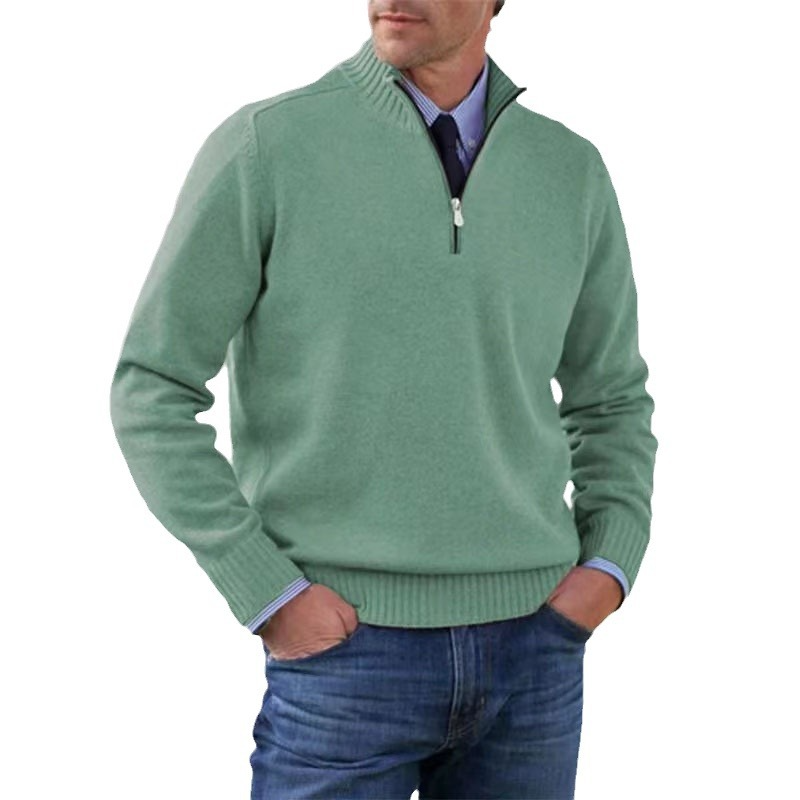 Homme portant un pull vert à col zippé, manches longues, sur une chemise bleue, avec un jean. Mode masculine élégante et décontractée.