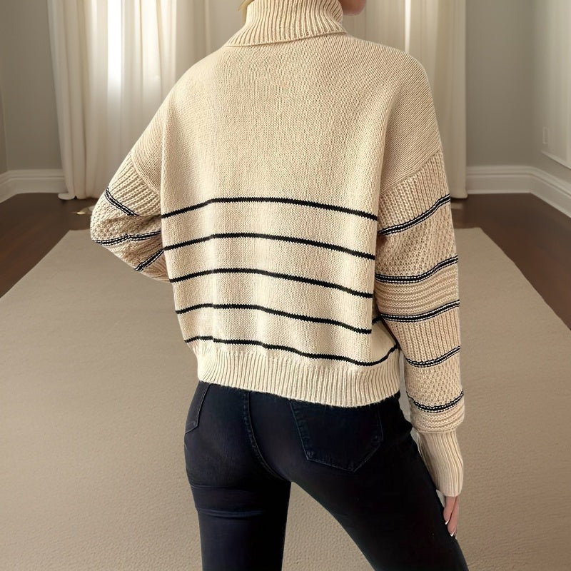 Femme portant un pull beige à col roulé avec rayures noires, manches longues, debout dans une pièce lumineuse. Mode automne-hiver, style décontracté.