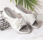 Sandales blanches pour femmes avec motif floral, talon compensé, sur fond de feuilles vertes et grille noire. Chaussures d'été élégantes et confortables.