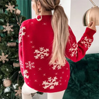 Femme portant un pull rouge avec motifs flocons de neige, debout près d'un sapin de Noël décoré. Mode hiver, tenue festive, ambiance Noël.