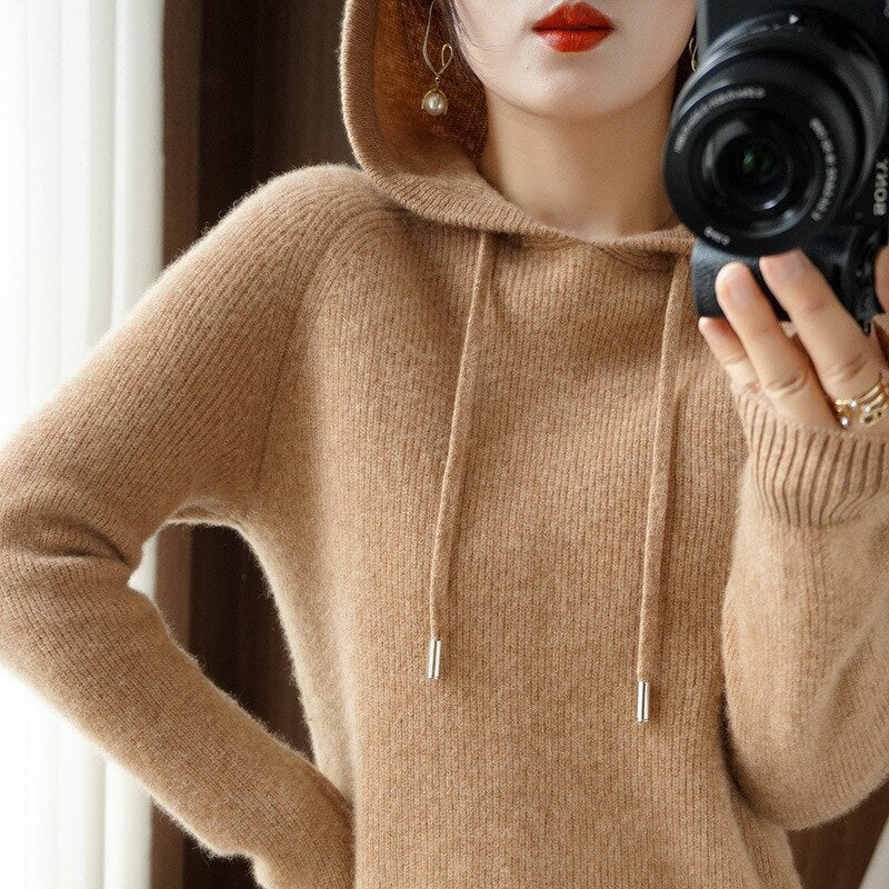 Femme en pull à capuche beige en laine, tenant un appareil photo. Mode automne-hiver, style décontracté, photographie, accessoires élégants.