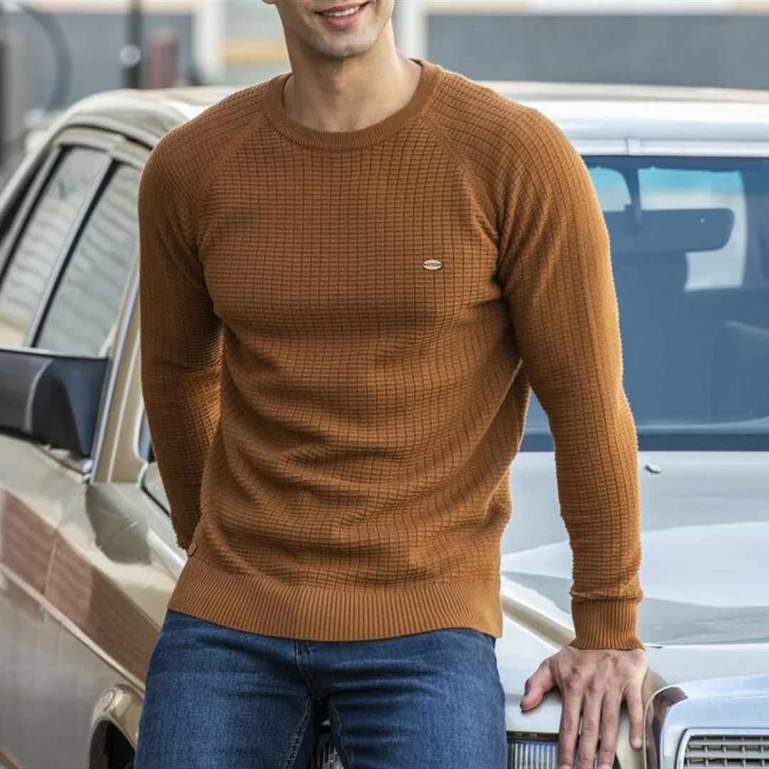 Homme en pull marron texturé, appuyé sur une voiture classique beige, portant un jean bleu. Mode automne, style décontracté, rue urbaine.