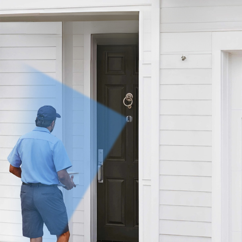 Livreur en uniforme bleu approchant une porte d'entrée noire avec sonnette vidéo, concept de sécurité à domicile, surveillance intelligente, livraison colis.