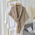 Châle en tricot beige avec motif torsadé, accroché sur cintre doré, à côté d'une chemise blanche. Accessoire mode élégant et tendance.