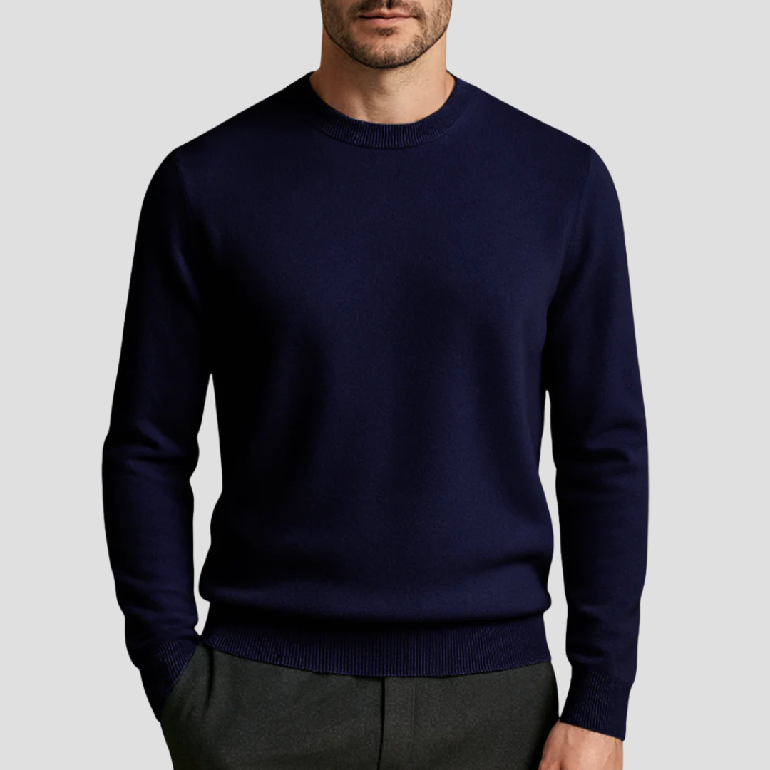 Homme portant un pull bleu marine élégant, col rond, manches longues, sur fond gris. Mode masculine, style décontracté chic, vêtement automne-hiver.