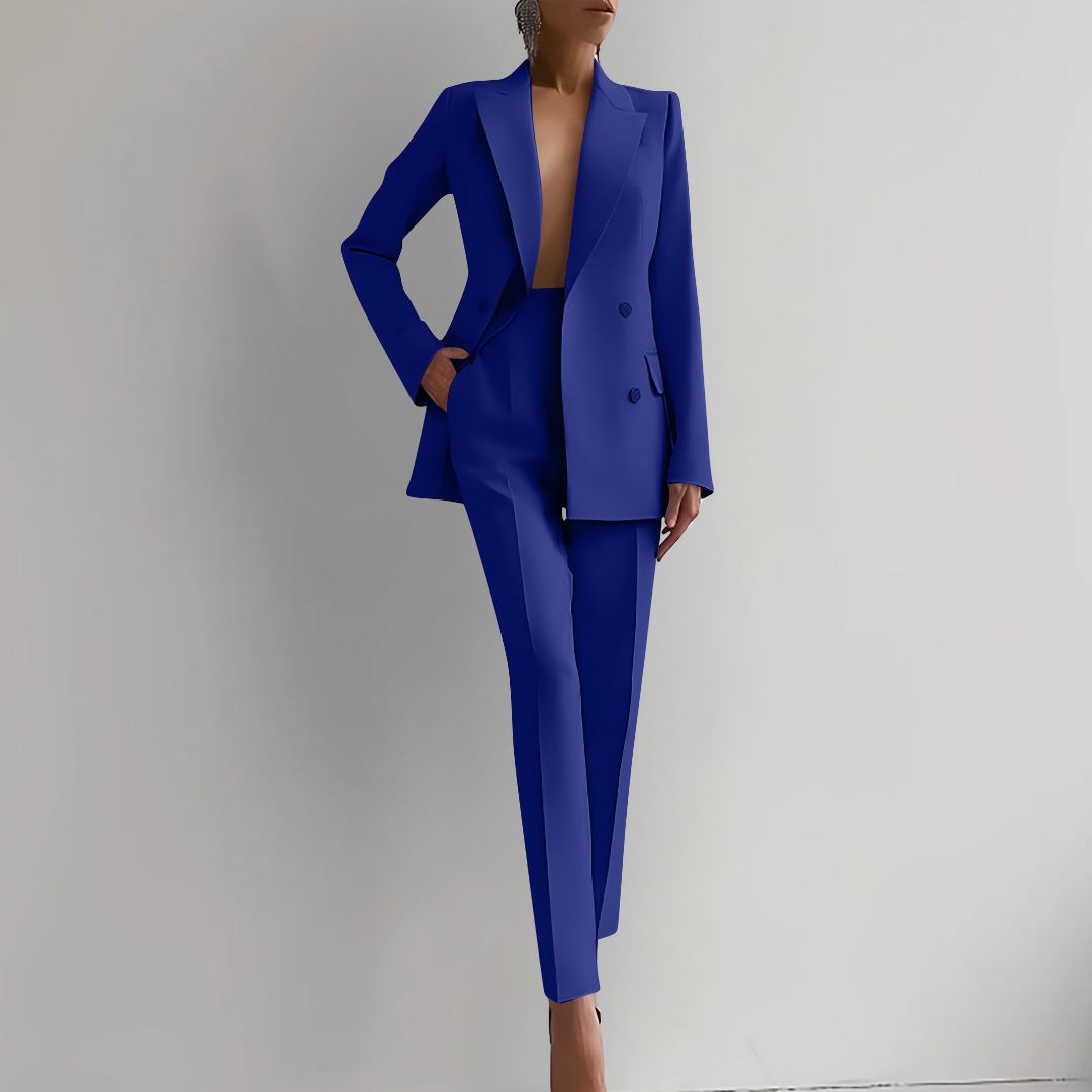 Femme en tailleur bleu électrique, pose élégante contre un mur blanc. Mode féminine, style professionnel, tendance vestimentaire moderne.