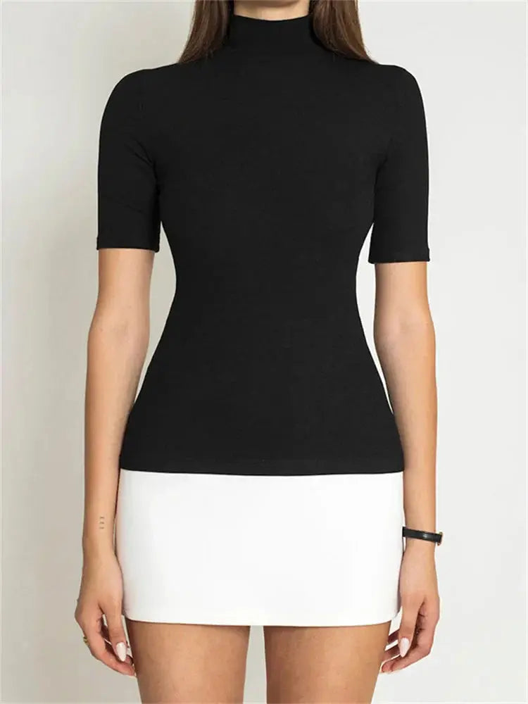Femme portant un haut noir à manches courtes et col montant, jupe blanche courte, style minimaliste, mode élégante et moderne.