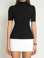 Femme portant un haut noir à manches courtes et col montant, jupe blanche courte, style minimaliste, mode élégante et moderne.