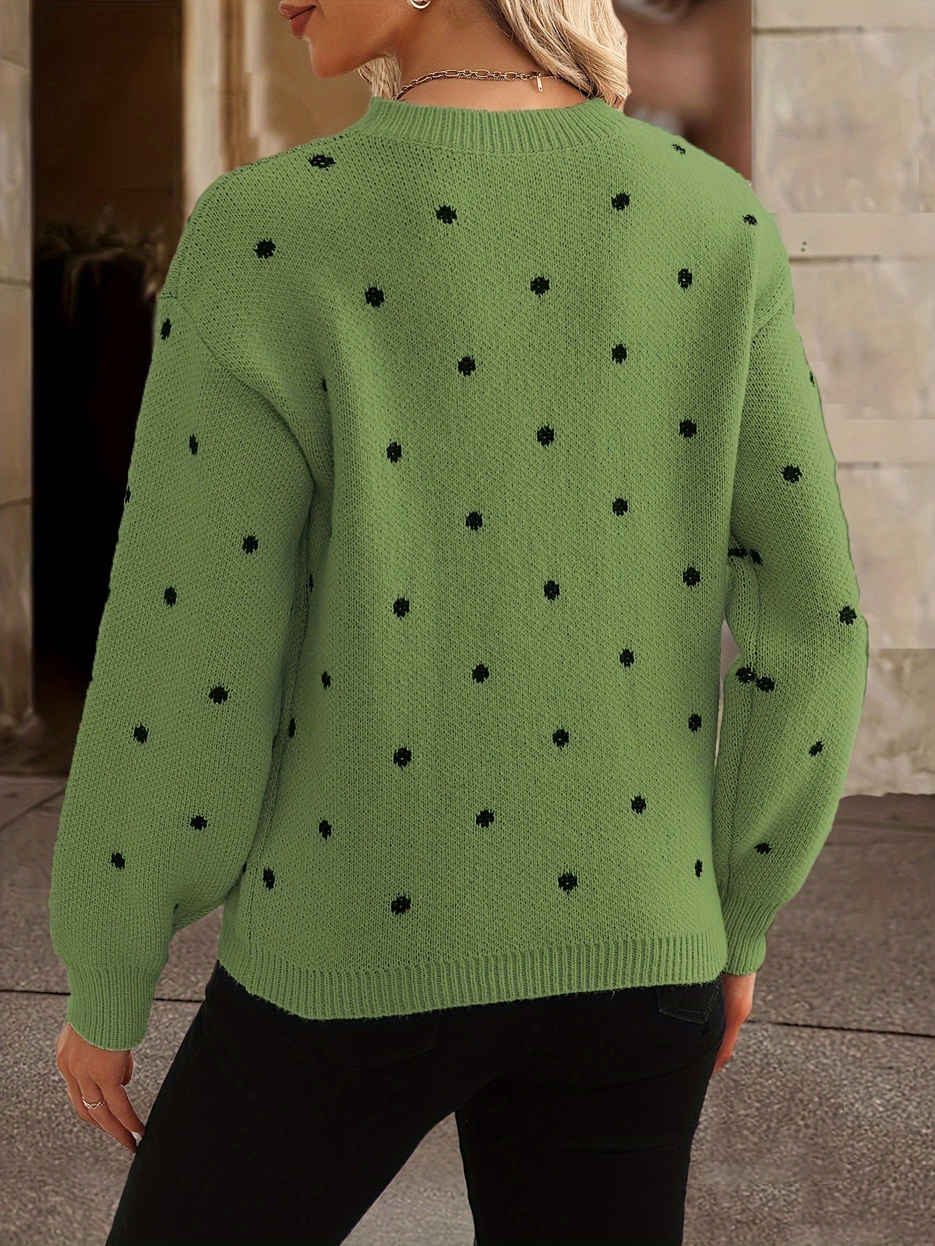 Femme portant un pull vert à pois noirs, manches longues, col rond, style décontracté, arrière-plan urbain. Mode automne-hiver tendance.