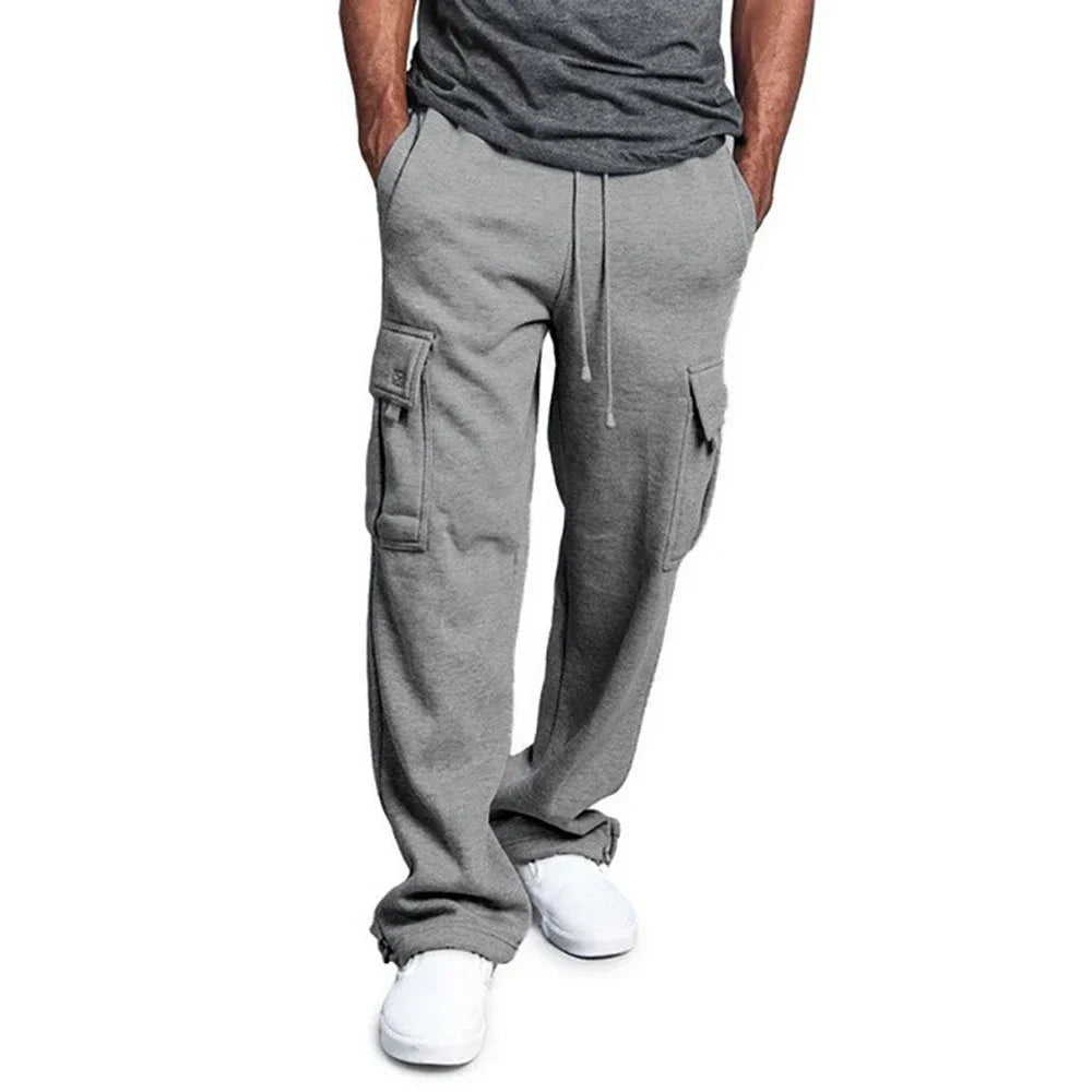 Pantalon cargo gris pour homme avec poches latérales, cordon de serrage, porté avec un t-shirt gris et des baskets blanches. Mode décontractée masculine.