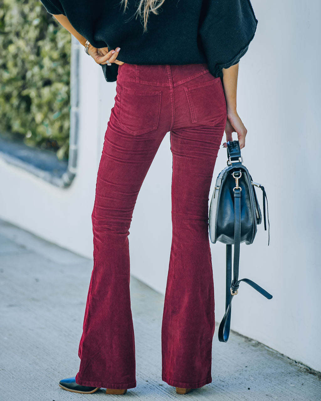 Femme portant un pantalon patte d'éléphant rouge, chemise noire, tenant un sac à main noir. Mode rétro, style décontracté, tendance automne.
