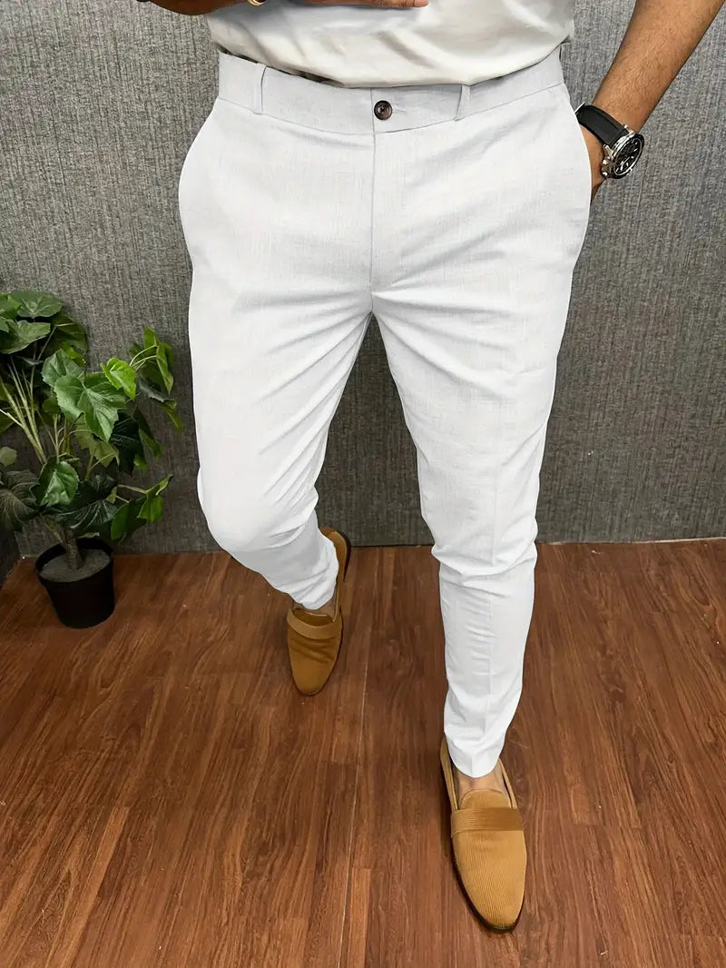 Pantalon blanc élégant pour homme, porté avec des mocassins marron, sur fond de sol en bois et plante verte. Mode masculine chic et moderne.