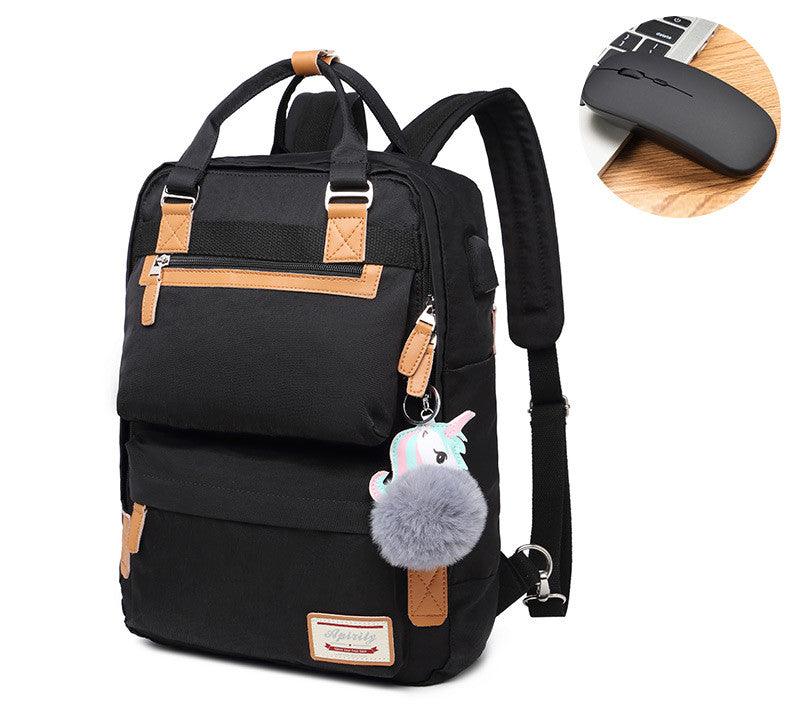Sac à dos noir élégant avec détails en cuir marron, pompon gris et porte-clés licorne, accompagné d'une souris sans fil noire sur fond bois.