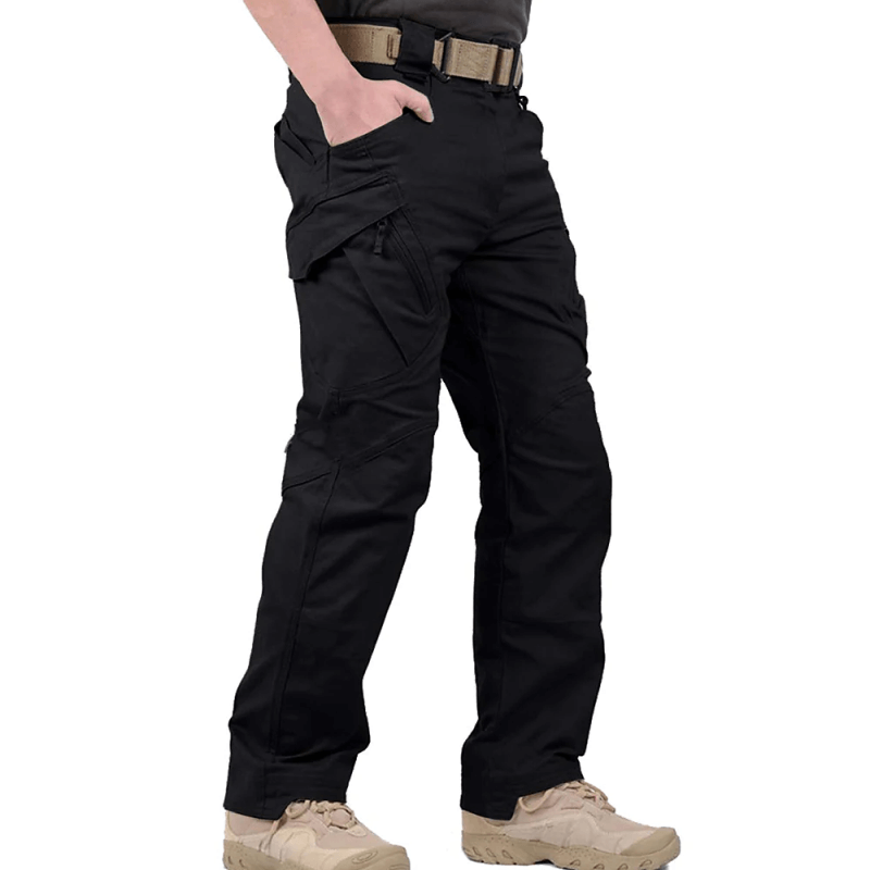 Pantalon tactique noir pour homme avec poches multiples, ceinture beige et chaussures de randonnée. Idéal pour activités extérieures et survie.