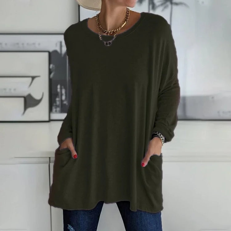 Femme portant un pull oversize vert foncé avec poches, collier doré, et jeans. Mode décontractée, tendance automne, style chic et confortable.