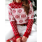 Femme portant un pull de Noël rouge à motifs flocons de neige blancs, assise devant un sapin décoré. Mode hiver, tenue festive élégante.