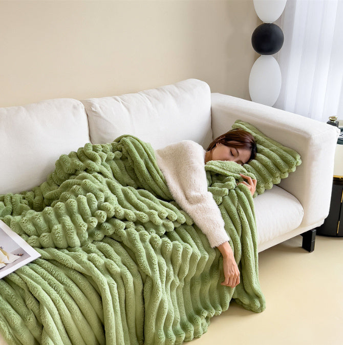 Femme endormie sur canapé blanc avec couverture en fausse fourrure verte, coussin assorti, intérieur moderne, ambiance cosy et détente.