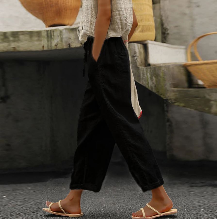 Pantalon noir ample en lin pour femme, style décontracté, avec poches, porté avec des sandales blanches, ambiance estivale et urbaine.