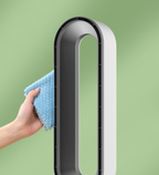 Main propre nettoyant un ventilateur sans pales moderne avec un chiffon bleu sur fond vert. Design élégant, technologie innovante, entretien facile.