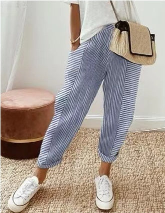 Femme portant un pantalon rayé bleu et blanc, t-shirt blanc, baskets blanches, sac à main en paille. Mode décontractée, tendance estivale.