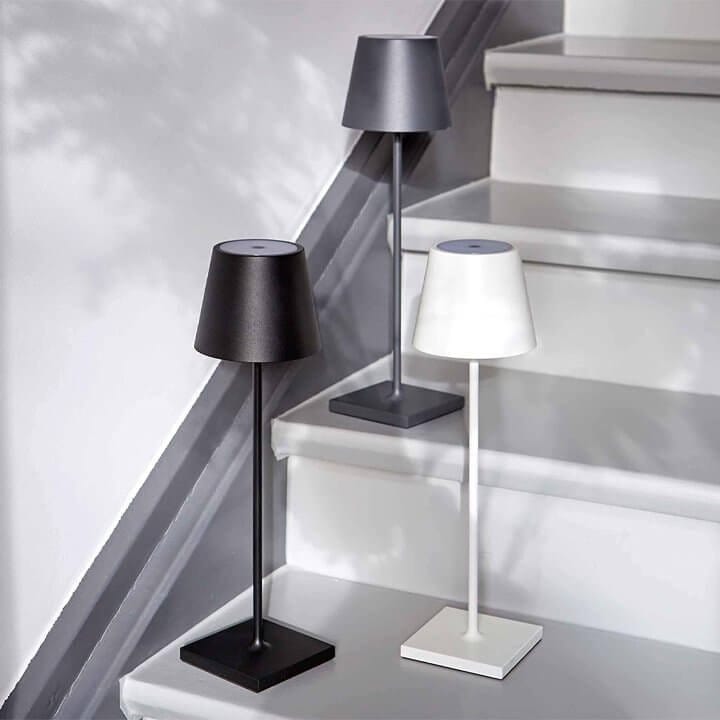 Trois lampes de table modernes en métal noir, gris et blanc posées sur des marches d'escalier, éclairage intérieur design minimaliste.