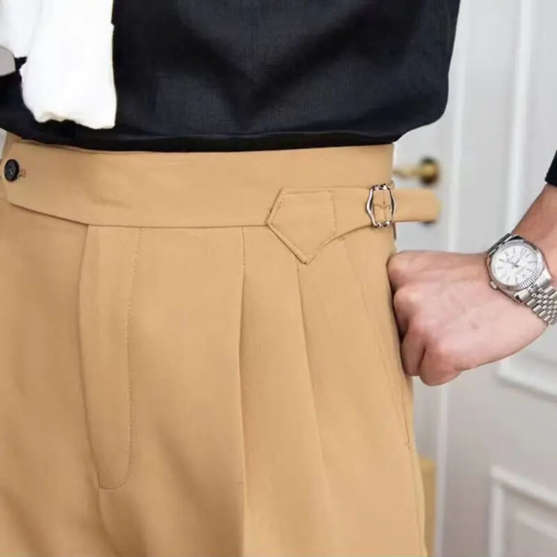 Pantalon beige élégant avec boucle ajustable, porté avec chemise noire. Montre-bracelet argentée visible. Mode masculine chic et moderne.