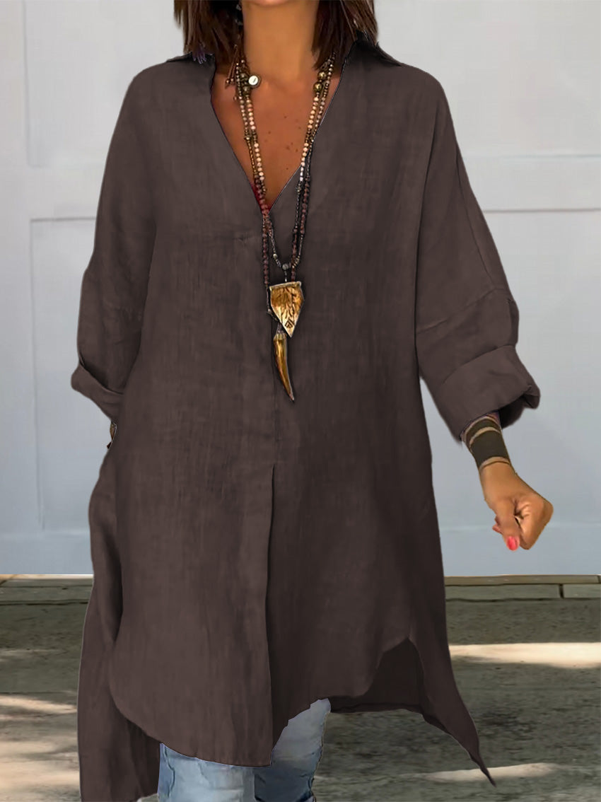 Femme portant une tunique marron ample, col en V, manches longues retroussées, avec collier pendentif. Mode décontractée, style bohème chic.