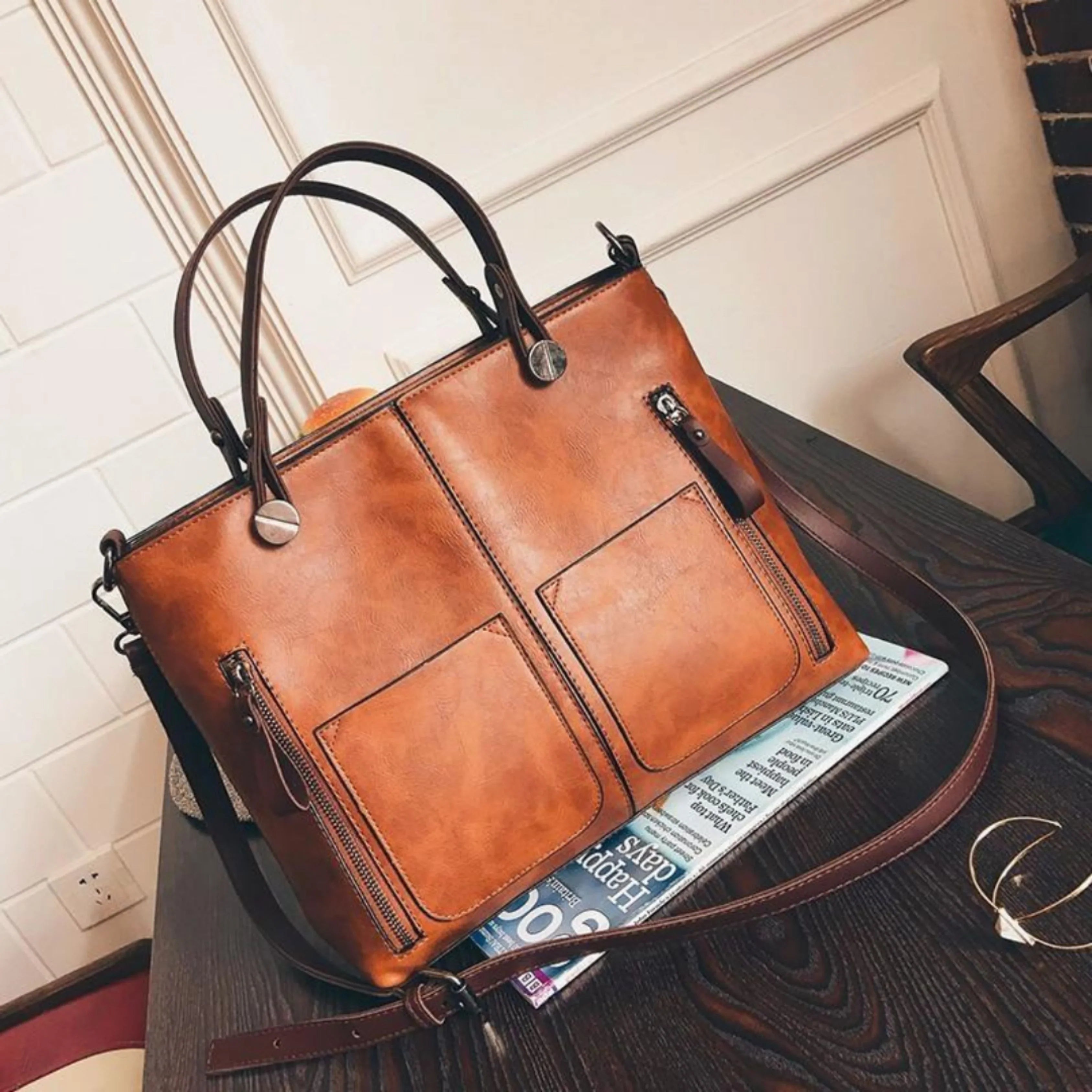 Sac à main en cuir marron sur une table en bois, avec deux poches avant et une bandoulière. Accessoire de mode élégant pour femmes.
