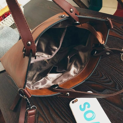 Sac à main en cuir marron ouvert sur une table en bois sombre, montrant l'intérieur doublé de tissu beige. Smartphone blanc à côté.