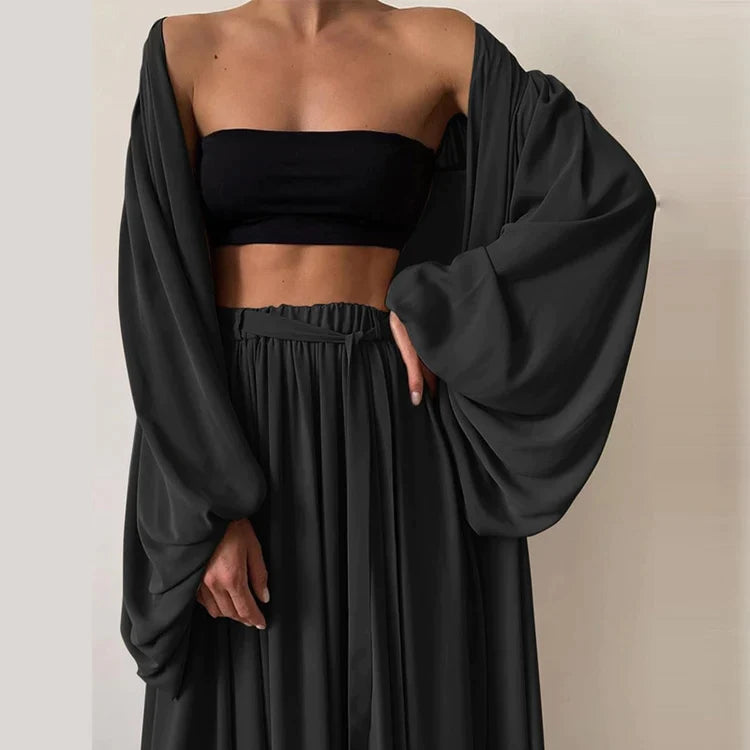 Femme portant un ensemble noir élégant avec haut bandeau et jupe longue fluide, manches amples. Mode chic, tenue moderne, style minimaliste.