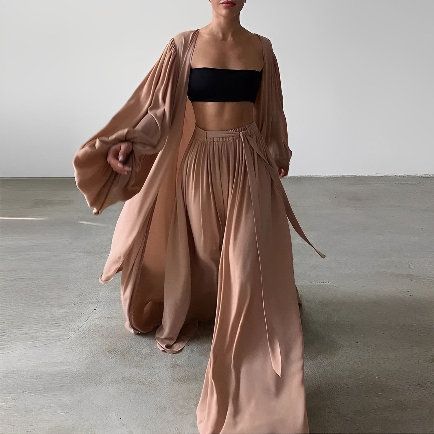 Femme portant un ensemble fluide beige, composé d'un long kimono et d'un pantalon ample, avec un haut bandeau noir. Mode élégante et minimaliste.