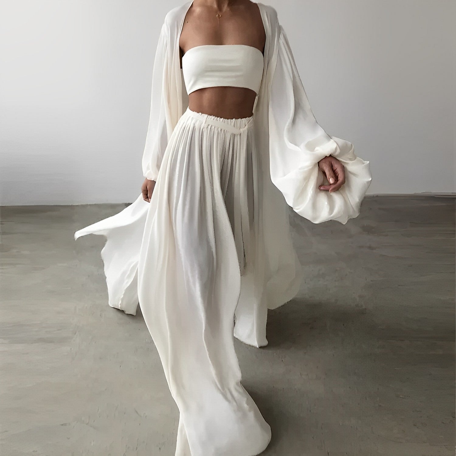 Femme en tenue blanche élégante, robe fluide et top bandeau, marchant sur sol en béton. Mode minimaliste, style chic et moderne.