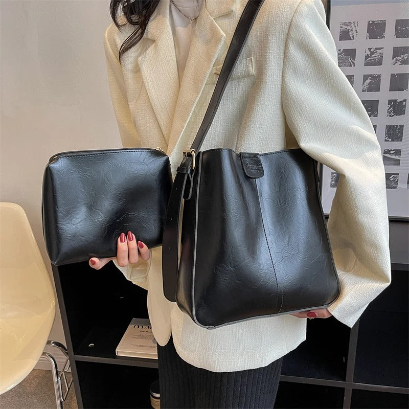Femme tenant un sac à main en cuir noir et une pochette assortie, vêtue d'un blazer beige. Accessoires de mode élégants et tendance.