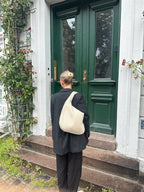 Femme en noir avec sac à main beige devant une porte verte, entourée de plantes grimpantes. Mode urbaine, style décontracté, architecture classique.