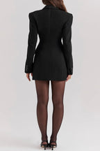 Femme en robe blazer noire élégante, manches longues, vue de dos, portant des collants noirs et des talons, style chic et moderne.