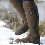 Bottes d'équitation en cuir marron sur neige, logo visible, idéales pour l'hiver et l'équitation. Chaussures robustes et élégantes pour cavaliers.