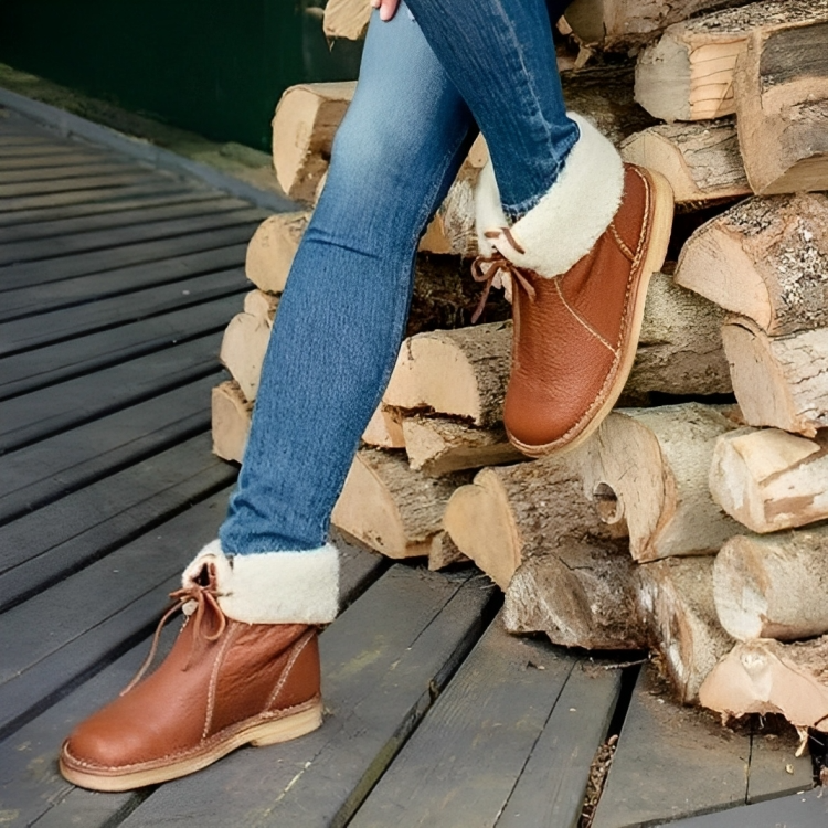 Bottes en cuir marron avec doublure en fourrure, portées avec un jean, posées sur des bûches de bois. Mode automne-hiver, chaussures confortables.