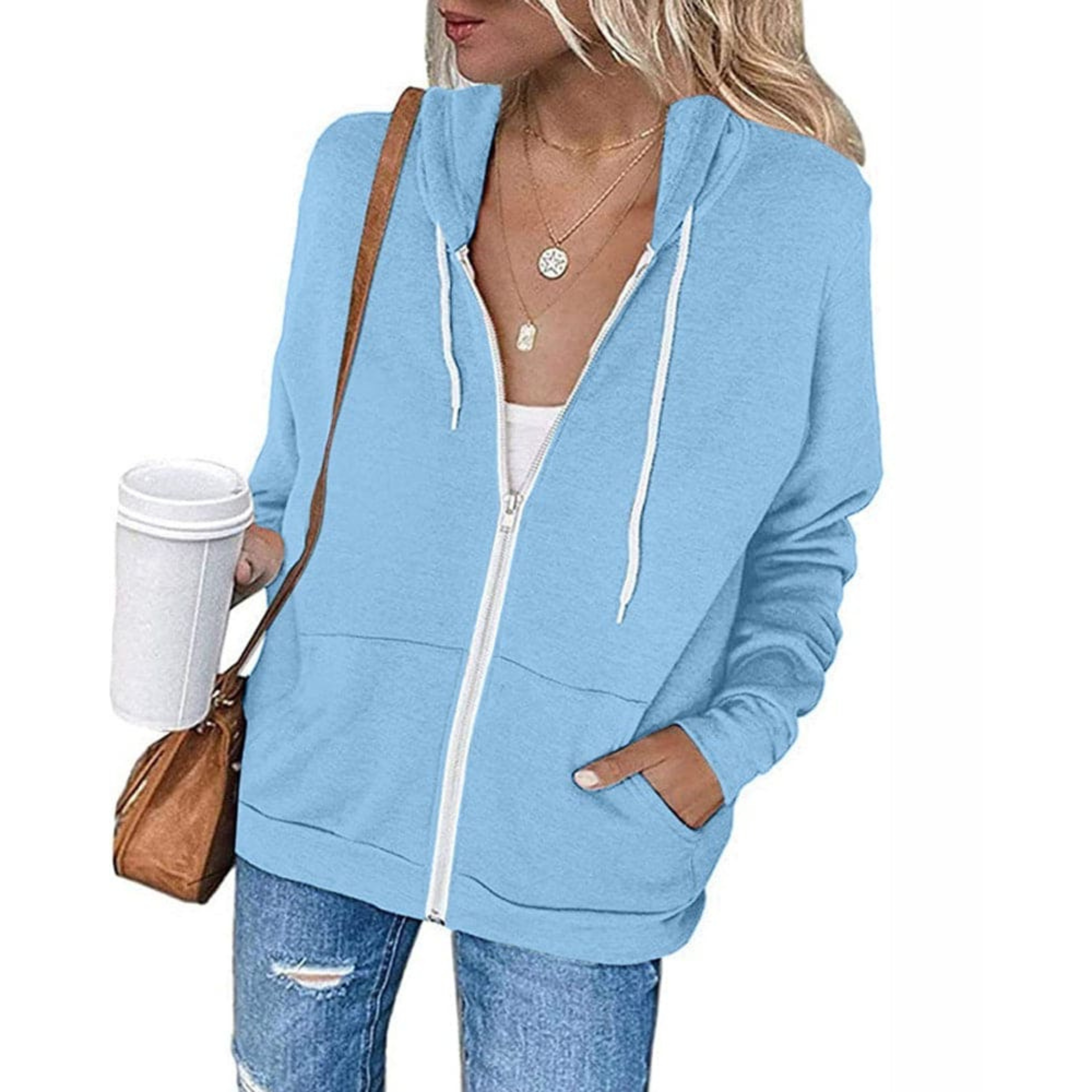 Femme portant un sweat à capuche bleu clair, jeans décontracté, sac marron, tenant un gobelet blanc. Mode décontractée, style urbain, vêtements tendance.