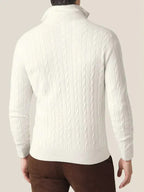 Homme portant un pull torsadé blanc en laine, manches longues, col montant, sur fond beige. Mode masculine élégante, tenue automne-hiver.