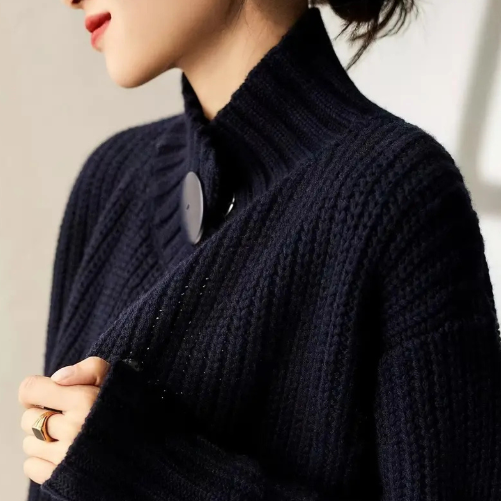 Femme portant un pull en maille côtelée bleu marine avec col montant et bouton décoratif, style élégant et moderne, mode automne-hiver.