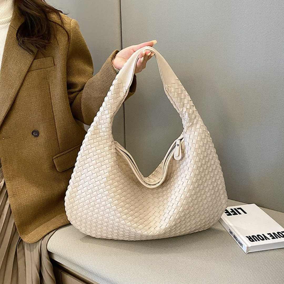 Sac à main tissé beige élégant, porté par une femme en manteau marron, posé sur un banc avec un livre. Accessoire mode tendance et chic.