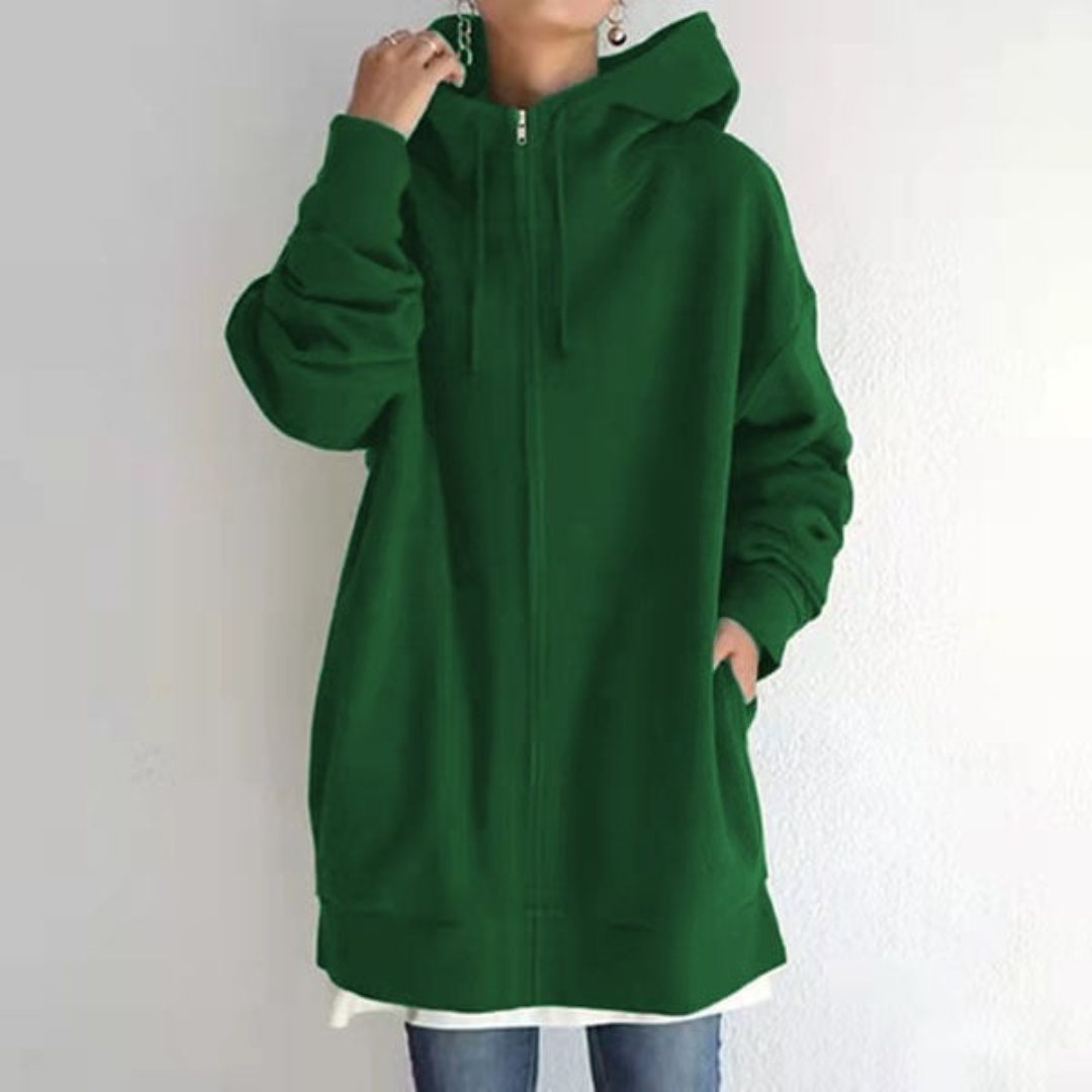 Femme portant un sweat à capuche vert ample, fermeture éclair, poches, sur fond blanc. Mode décontractée, tendance automne-hiver, style urbain.