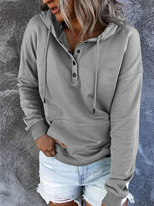 Femme portant un sweat à capuche gris avec boutons, manches longues, poche kangourou, associé à un short en jean déchiré. Mode décontractée tendance.