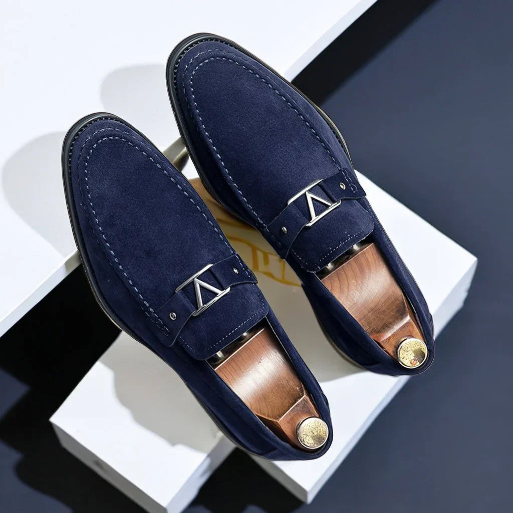 Mocassins en daim bleu marine élégants pour hommes avec boucle métallique, posés sur fond blanc. Chaussures de luxe, mode masculine, style moderne.