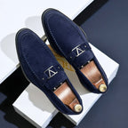 Mocassins en daim bleu marine élégants pour hommes avec boucle métallique, posés sur fond blanc. Chaussures de luxe, mode masculine, style moderne.