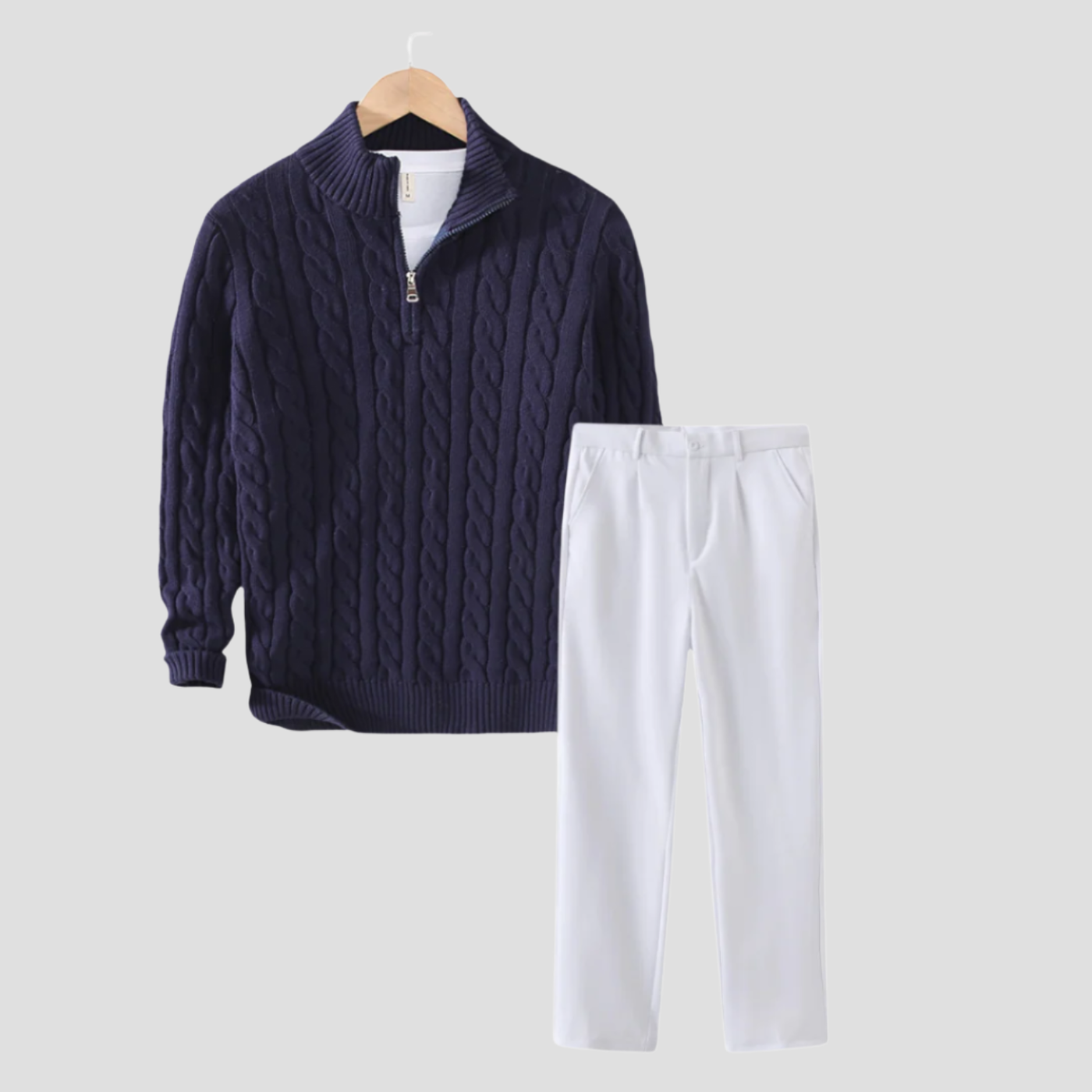Pull en maille torsadée bleu marine avec fermeture éclair et pantalon blanc élégant suspendus sur cintre. Mode automne-hiver, tenue chic décontractée.