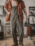Homme en salopette grise et chemise marron, tenant un pack de bières artisanales, dans un intérieur moderne avec décor industriel. Mode décontractée.