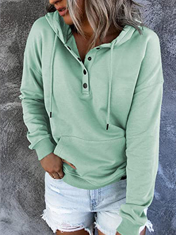 Femme portant un sweat à capuche vert menthe avec boutons, manches longues et poche kangourou, associé à un short en jean déchiré. Mode décontractée.