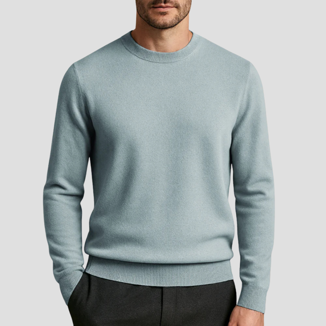 Homme portant un pull bleu clair en laine, col rond, manches longues, avec pantalon noir. Mode masculine élégante et décontractée.