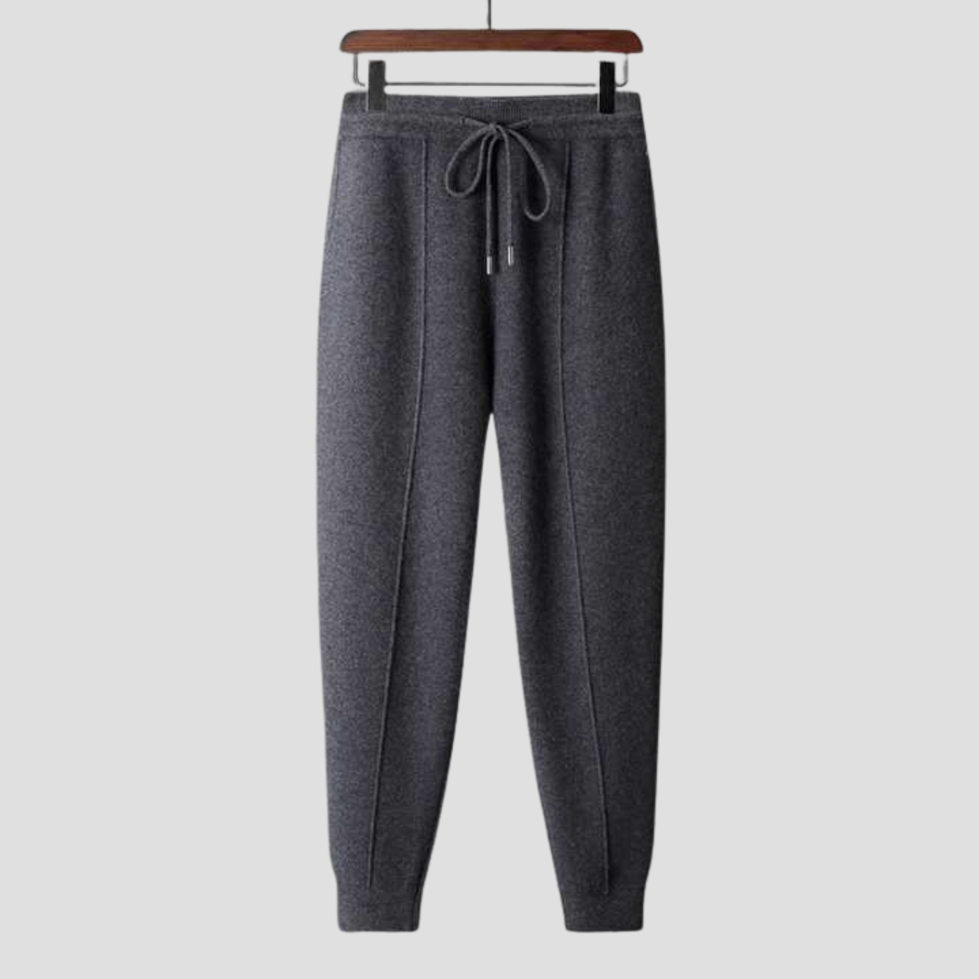 Pantalon de jogging gris foncé en laine, suspendu sur un cintre en bois, avec cordon de serrage, idéal pour confort et style décontracté.